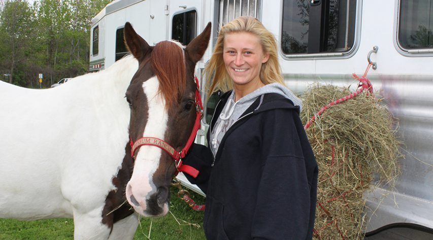 Student smiling while standing next to horse